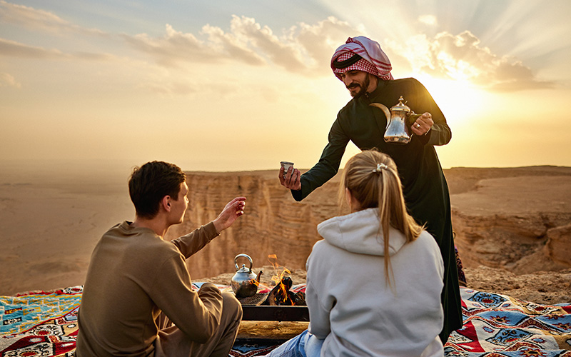 Man serving coffee to a couple on a cliff at the Edge of the World in Riyadh
