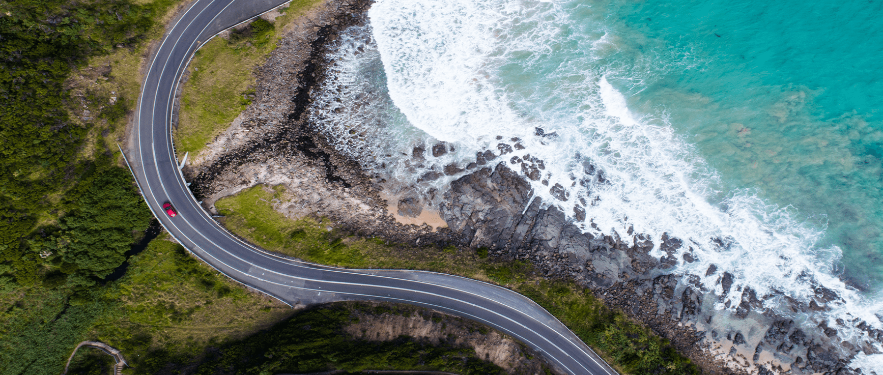 Car driving down winding road near the ocean